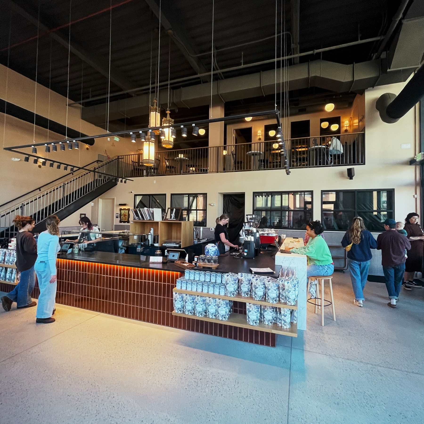 Methodical Coffee Columbia. A modern café interior features a central coffee bar with baristas serving customers and an upper level with additional seating.