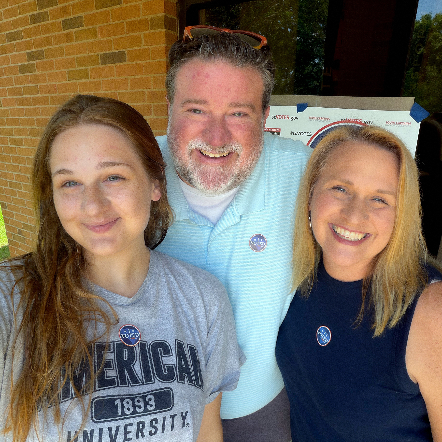 Three people are smiling at the camera, each wearing an I Voted sticker.