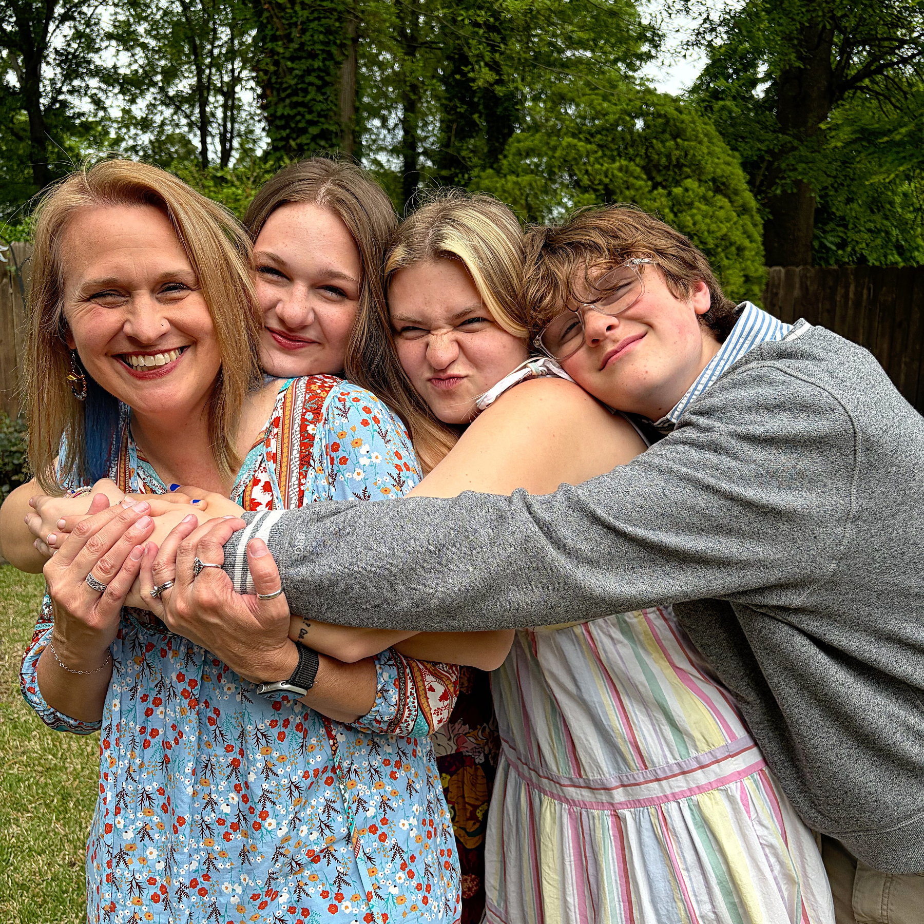 Four people are standing together outdoors, smiling and embracing each other.
